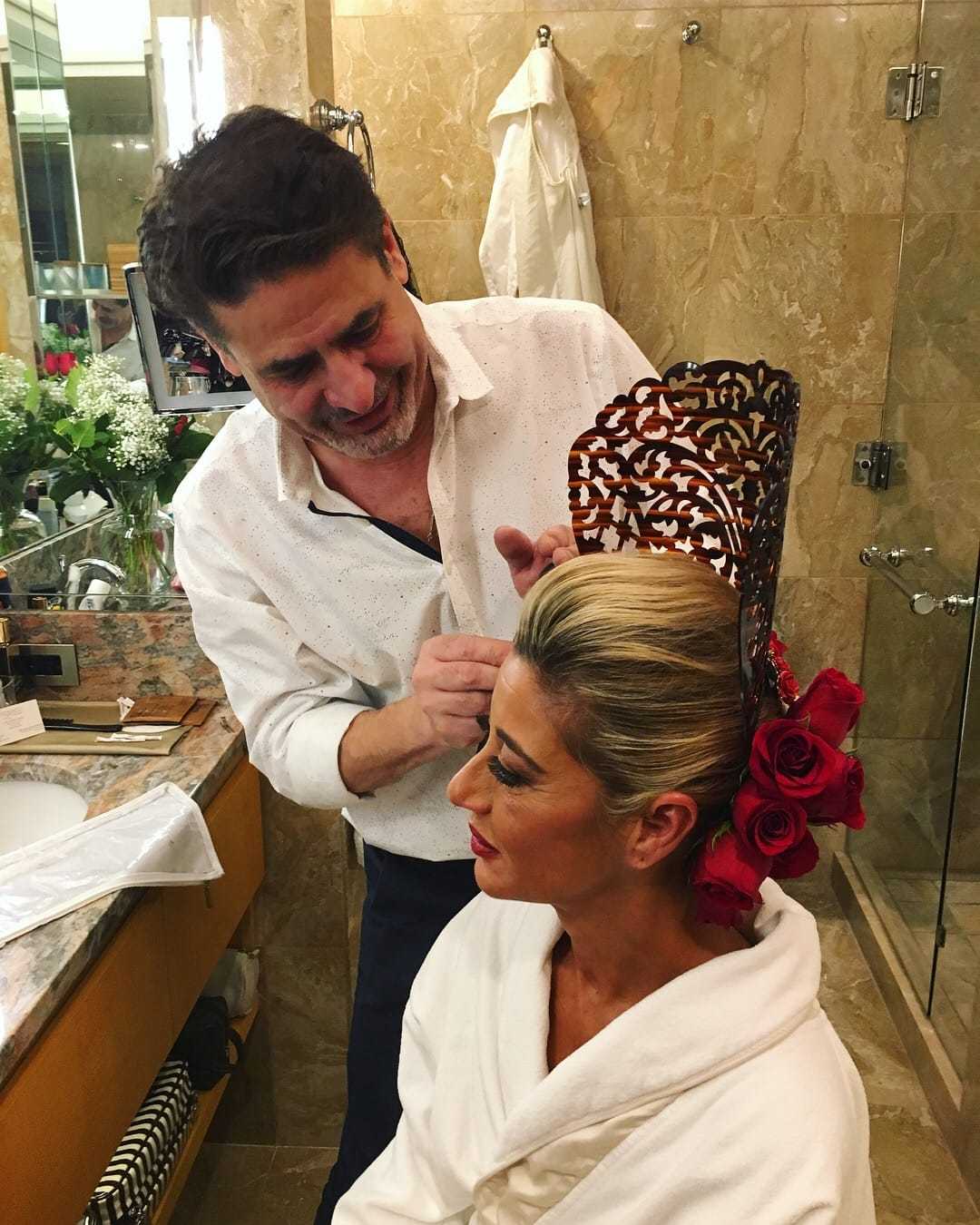 Hair stylist adjusts ornate headpiece with red roses for elegant woman in bathroom.