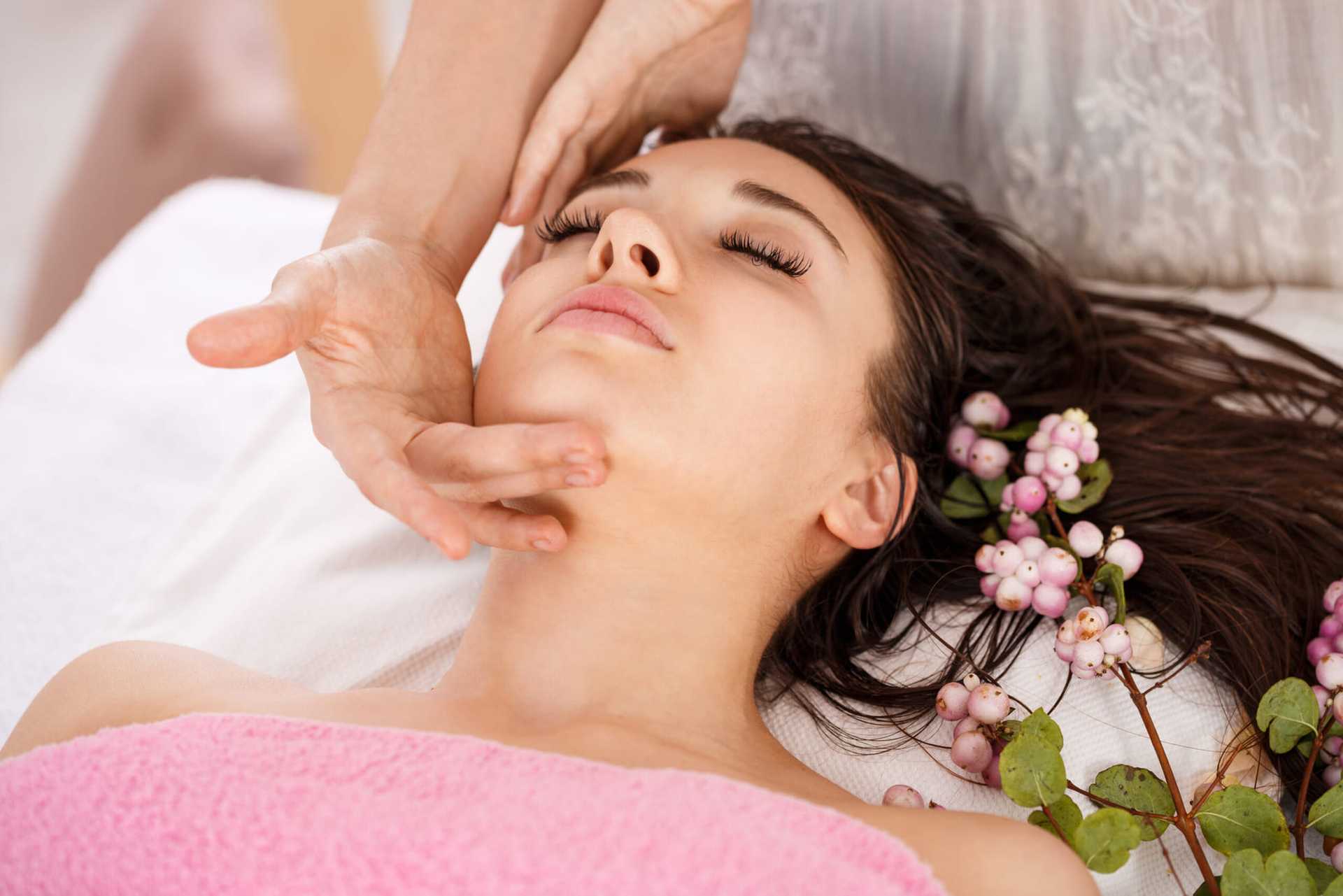 Woman enjoying a facial massage with pink flowers nearby.